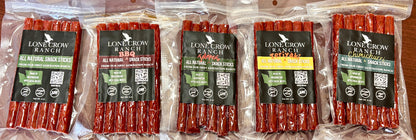 Five packages of Lone Crow Ranch all natural snack sticks arranged side by side on a wooden surface. The packages are clear plastic bags containing reddish-brown snack sticks, with black labels featuring the brand name and product details.